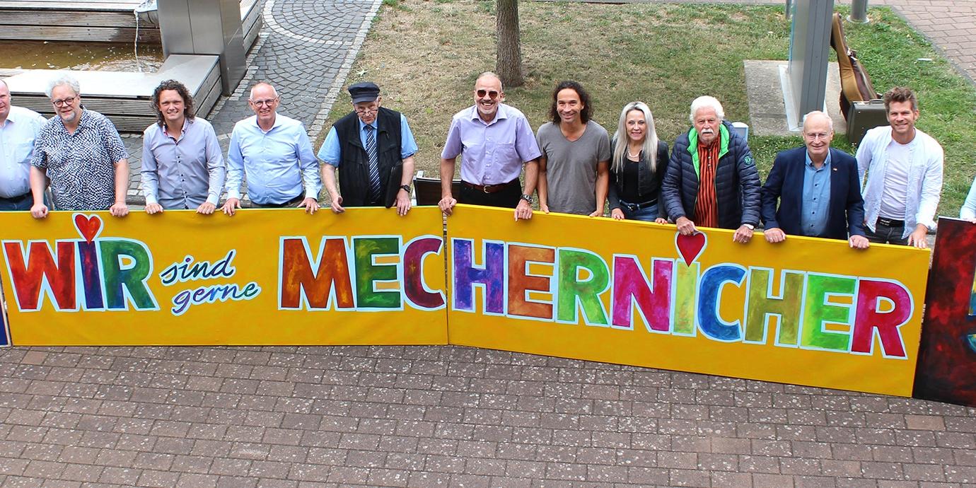 Viel Lust auf ein großes, fröhliches Stadtfest macht das knallbunte, vom Mechernicher Kurator Franz Kruse (5.v.r.) entworfene Kunstwerk, das die Musiker und Verantwortlichen nun vor dem Rathaus präsentierten.