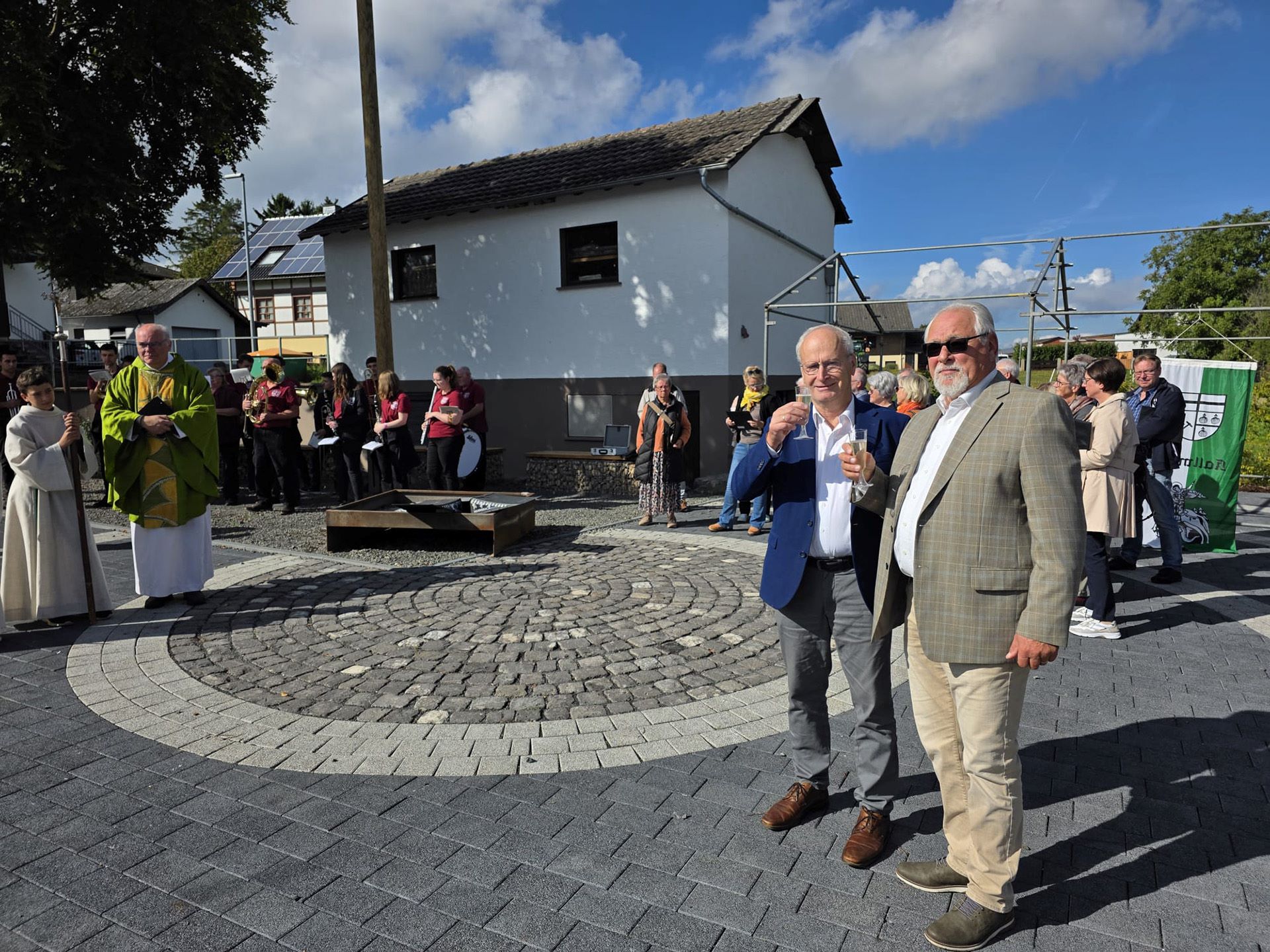 Sonnenschein und strahlende Gesichter bei Bürgermeister Hans-Peter Schick, Ortsbürgermeister Robert Ohlerth und den Kallmutherinnen und Kallmuthern, die nach der Einweihung durch Pfarrer Erik Pühringer auf ihren neuen Dorfplatz anstießen. (c) Foto: Privat/pp/Agentur ProfiPress