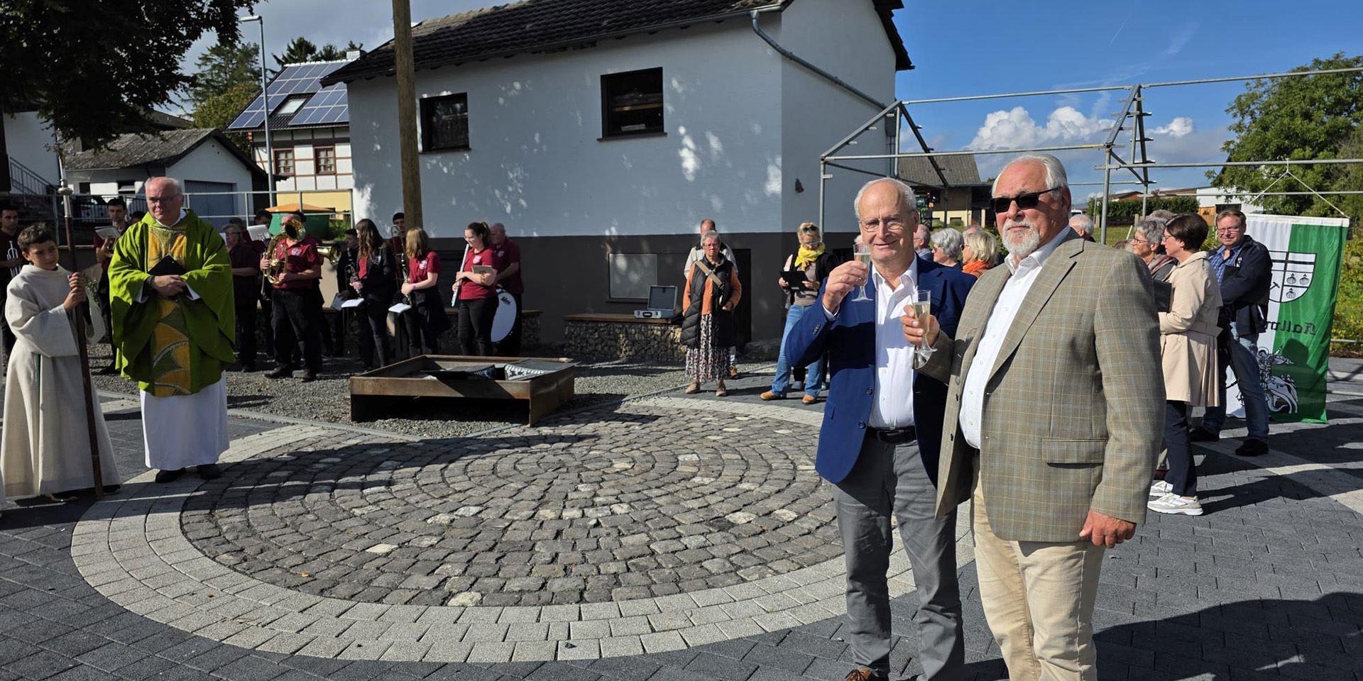 Sonnenschein und strahlende Gesichter bei Bürgermeister Hans-Peter Schick, Ortsbürgermeister Robert Ohlerth und den Kallmutherinnen und Kallmuthern, die nach der Einweihung durch Pfarrer Erik Pühringer auf ihren neuen Dorfplatz anstießen.