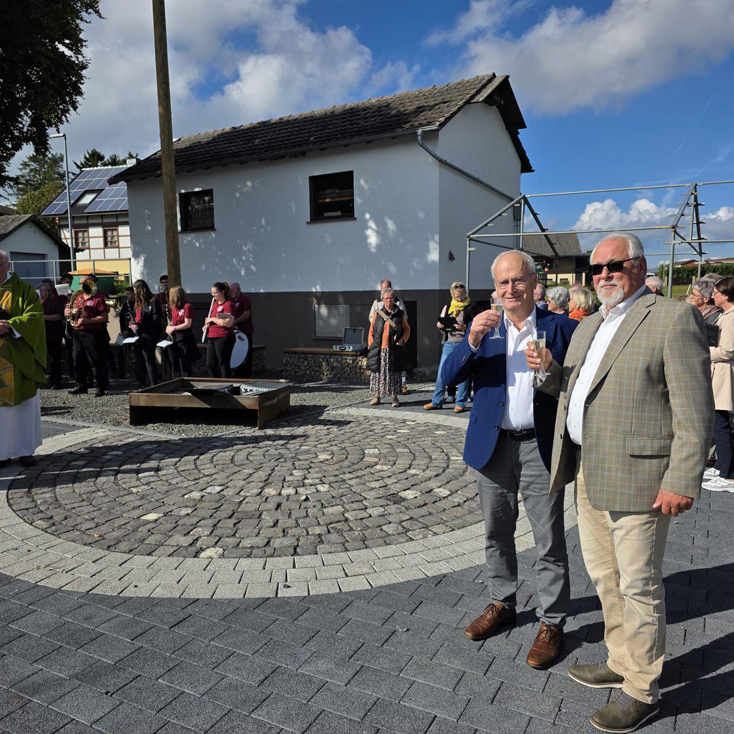 Sonnenschein und strahlende Gesichter bei Bürgermeister Hans-Peter Schick, Ortsbürgermeister Robert Ohlerth und den Kallmutherinnen und Kallmuthern, die nach der Einweihung durch Pfarrer Erik Pühringer auf ihren neuen Dorfplatz anstießen.