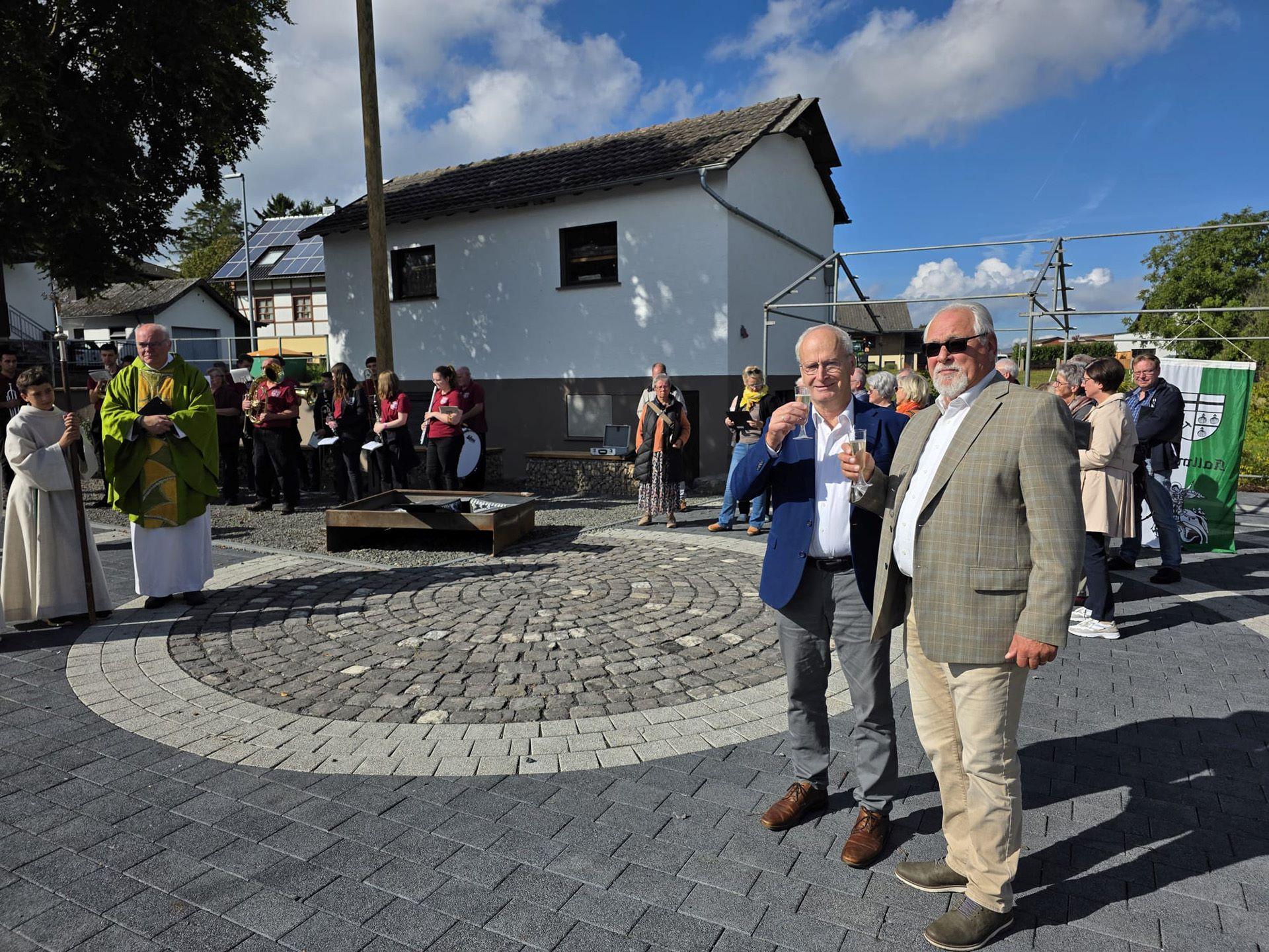 Sonnenschein und strahlende Gesichter bei Bürgermeister Hans-Peter Schick, Ortsbürgermeister Robert Ohlerth und den Kallmutherinnen und Kallmuthern, die nach der Einweihung durch Pfarrer Erik Pühringer auf ihren neuen Dorfplatz anstießen.