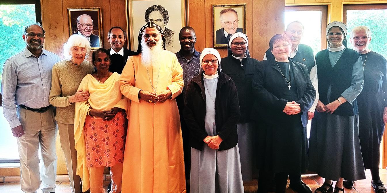Bischof Dr. Samuel Mar Irenios inmitten der Kommunität der Communio in Christo im Mechernicher Refektorium vor den Bildern der Gründerin Mutter Marie Therese, dem ersten Spiritual Hermann Walch und dem ersten Generalsuperior Karl-Heinz Haus.