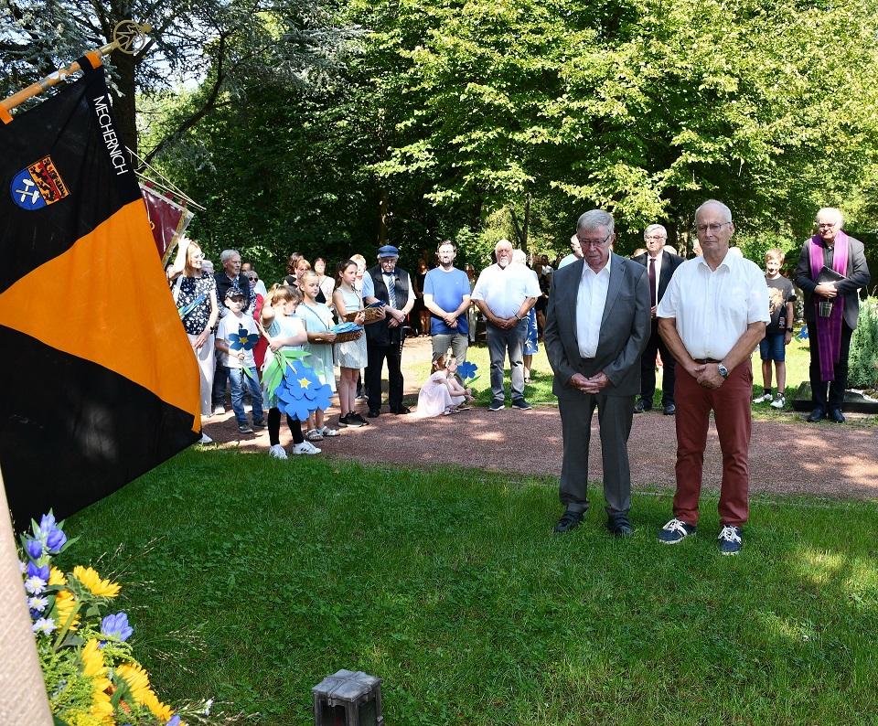 Bürgermeister Dr. Hans-Peter Schick (r.) und Ortsbürgermeister Günther Schulz haben einen Kranz für die Verstorbenen aus Mechernich niedergelegt, im Hintergrund links Kinder, die Papierblumen für die Gräber gebastelt hatten, rechts Pfarrer Erik Pühringer, in der Mitte hinten und links hinten die Vize-Bürgermeister Günter Kornell und Heinrich Schmitz.