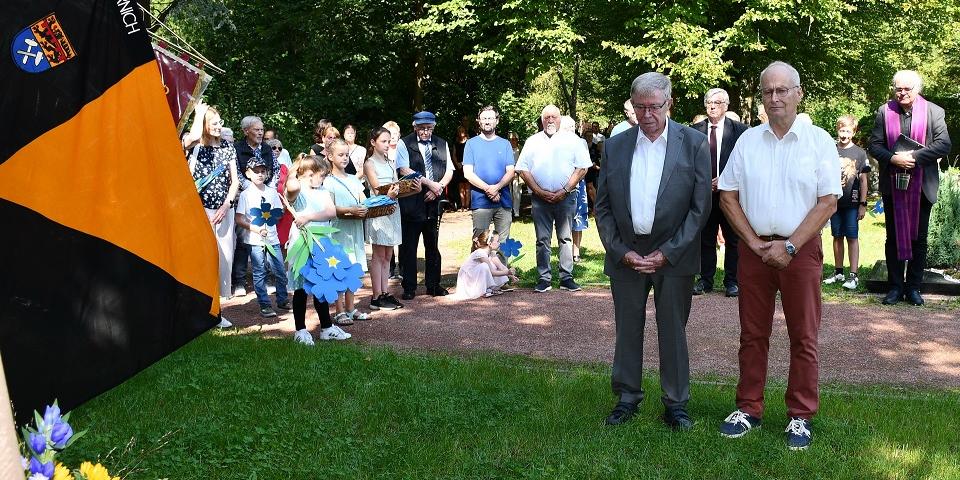 Bürgermeister Dr. Hans-Peter Schick (r.) und Ortsbürgermeister Günther Schulz haben einen Kranz für die Verstorbenen aus Mechernich niedergelegt, im Hintergrund links Kinder, die Papierblumen für die Gräber gebastelt hatten, rechts Pfarrer Erik Pühringer, in der Mitte hinten und links hinten die Vize-Bürgermeister Günter Kornell und Heinrich Schmitz.