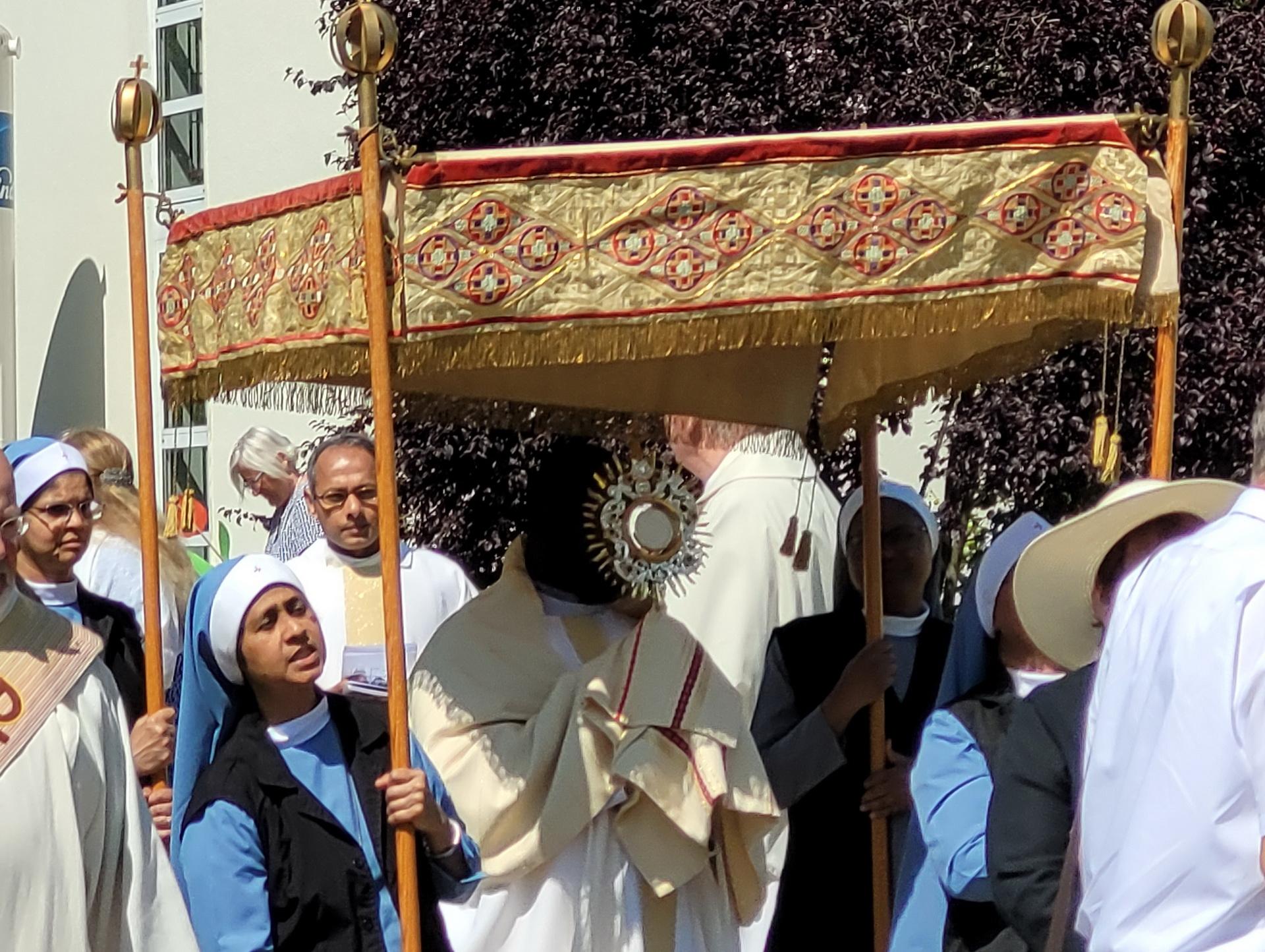 Der ugandische Priester Patrick Mwanguhya trägt das Allerheiligste in der Monstranz, indische Samaritan-Ordensschwestern tragen den „Himmel“, im Hintergrund Pfarrer Erik Pühringer und Generalsuperior Jaison Thazhathil.