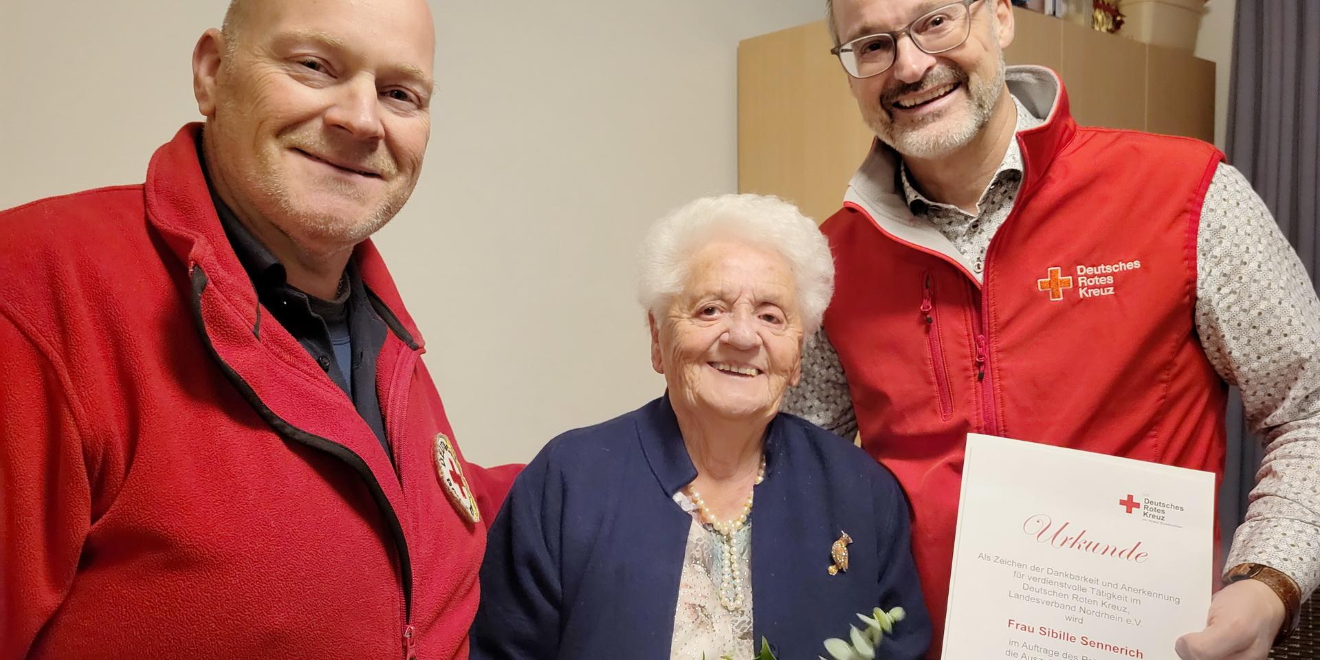 Ortsvereinsvorsitzender und Kreisgeschäftsführer Rolf Klöcker (r.) und Bereitschaftsleiter Sascha Suijkerland ehrten Sibille Sennerich mit Urkunde, Anstecknadel und Blumen.