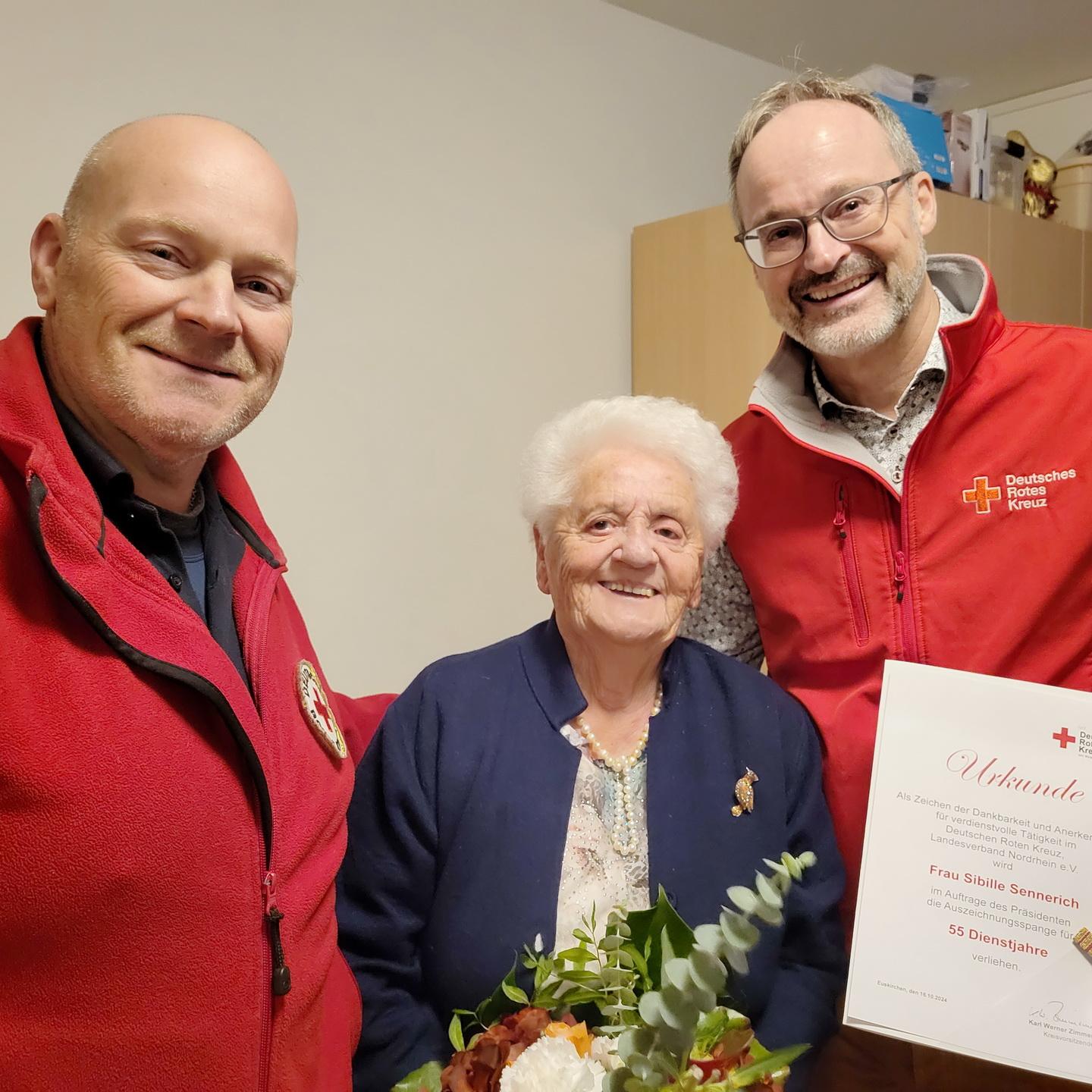 Ortsvereinsvorsitzender und Kreisgeschäftsführer Rolf Klöcker (r.) und Bereitschaftsleiter Sascha Suijkerland ehrten Sibille Sennerich mit Urkunde, Anstecknadel und Blumen.