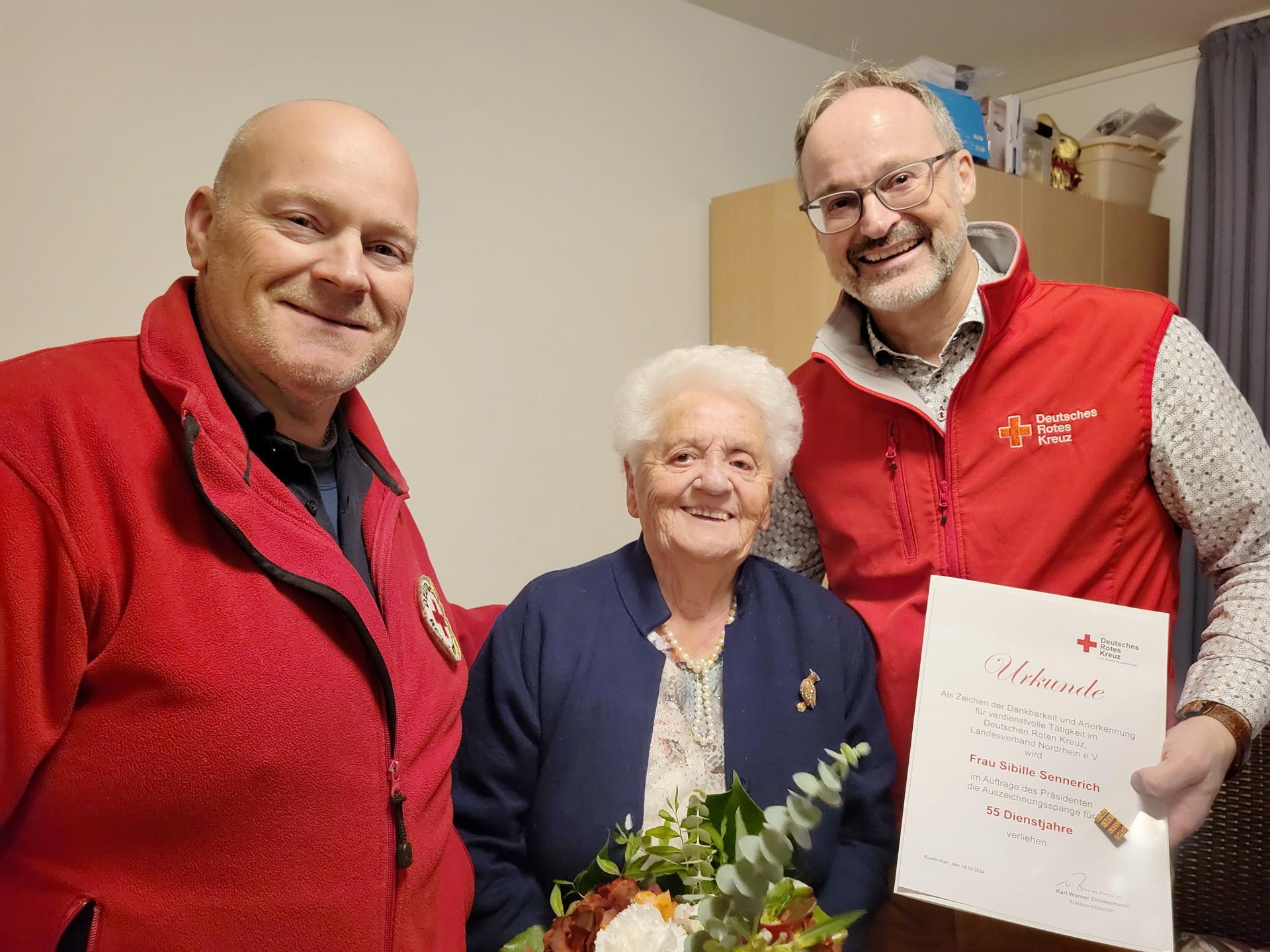 Ortsvereinsvorsitzender und Kreisgeschäftsführer Rolf Klöcker (r.) und Bereitschaftsleiter Sascha Suijkerland ehrten Sibille Sennerich mit Urkunde, Anstecknadel und Blumen.