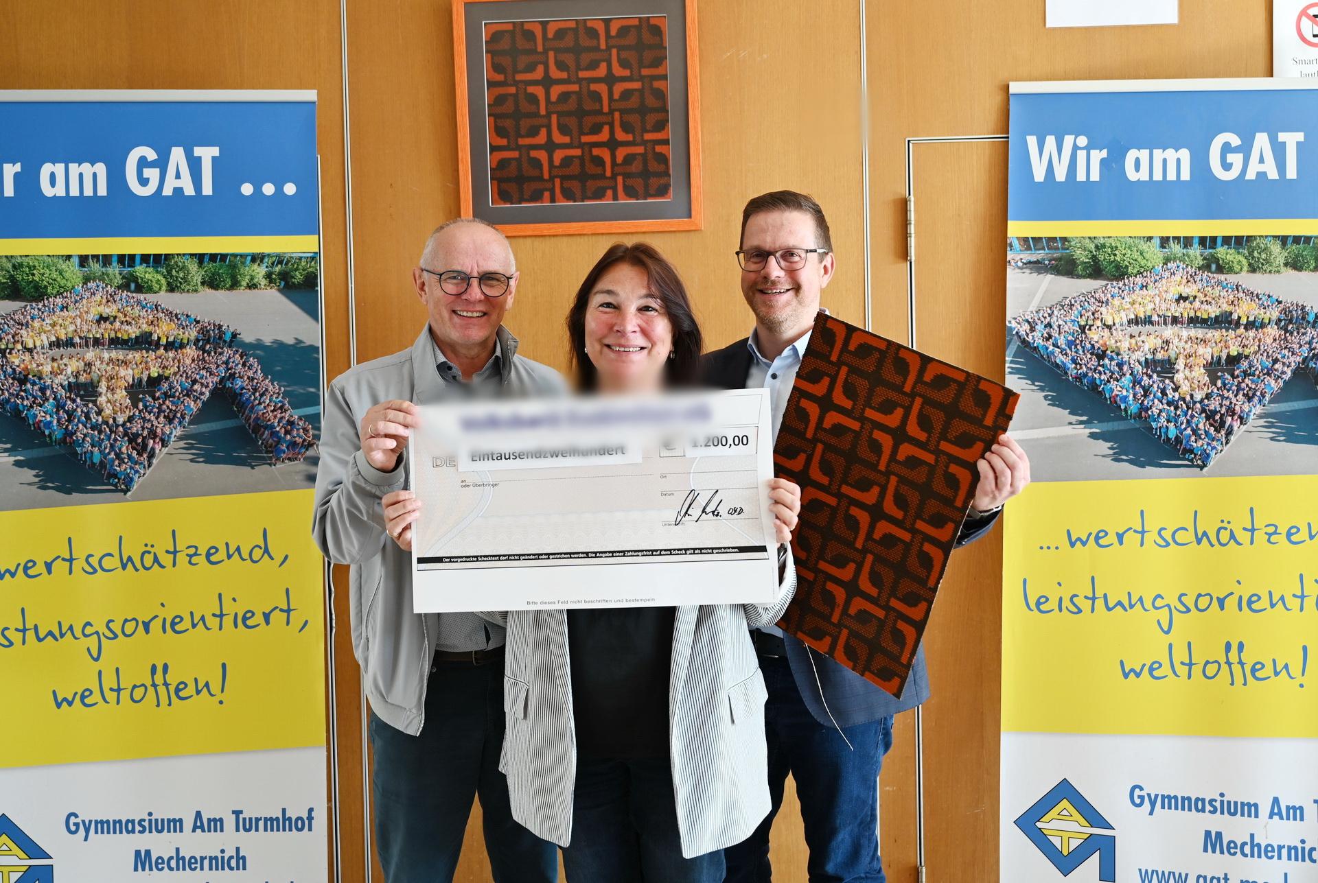 Karla Langer, Ralf Claßen (l.) und Micha Kreitz mit Teppichstücken aus der Aula und symbolischem Scheck bei der Spendenübergabe des Gymnasiums Am Turmhof an die Mechernich-Stiftung.