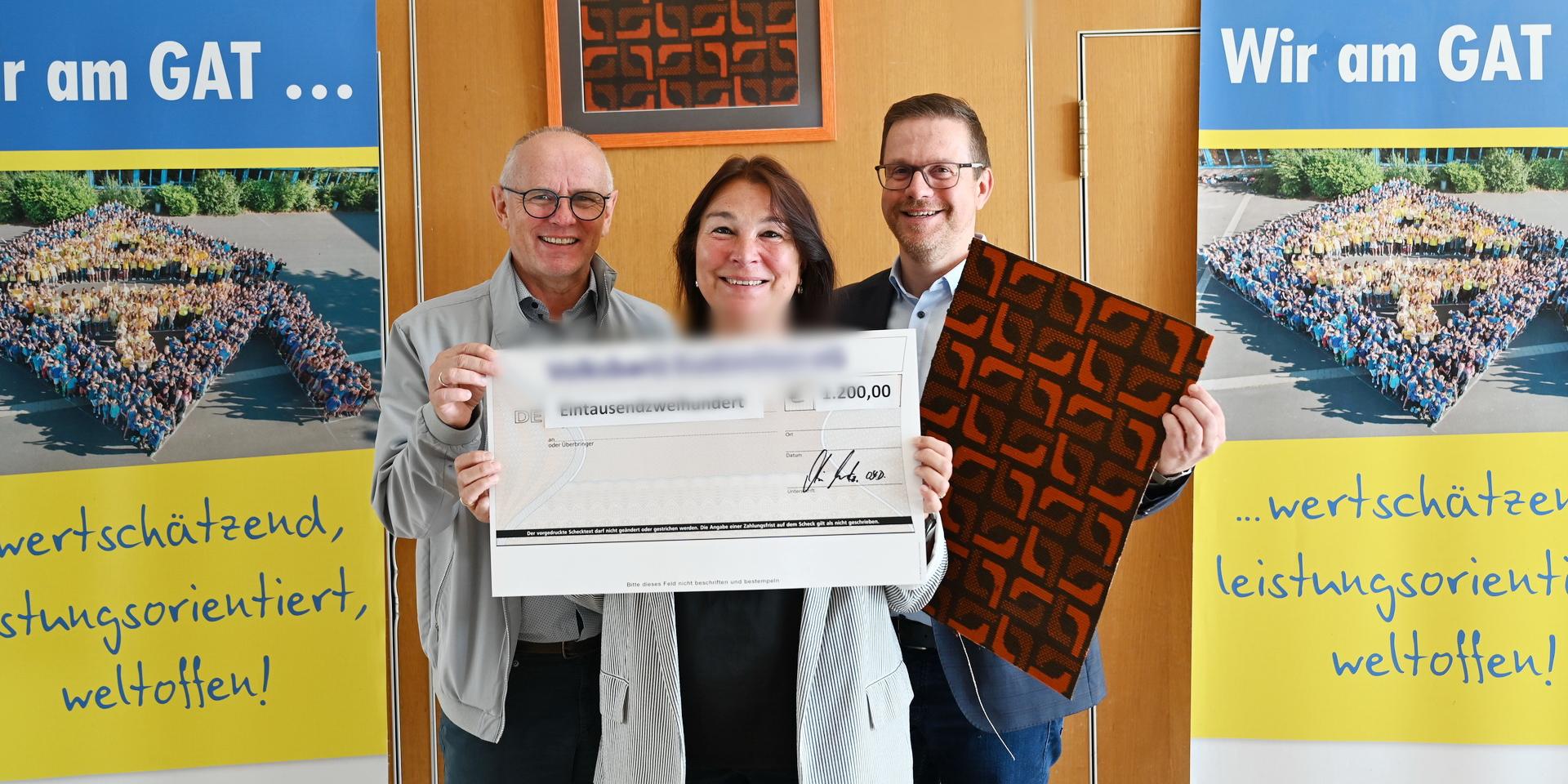 Karla Langer, Ralf Claßen (l.) und Micha Kreitz mit Teppichstücken aus der Aula und symbolischem Scheck bei der Spendenübergabe des Gymnasiums Am Turmhof an die Mechernich-Stiftung.