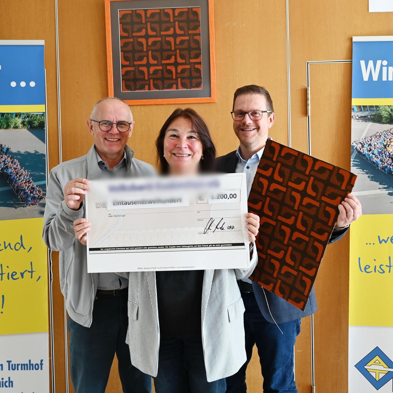 Karla Langer, Ralf Claßen (l.) und Micha Kreitz mit Teppichstücken aus der Aula und symbolischem Scheck bei der Spendenübergabe des Gymnasiums Am Turmhof an die Mechernich-Stiftung.