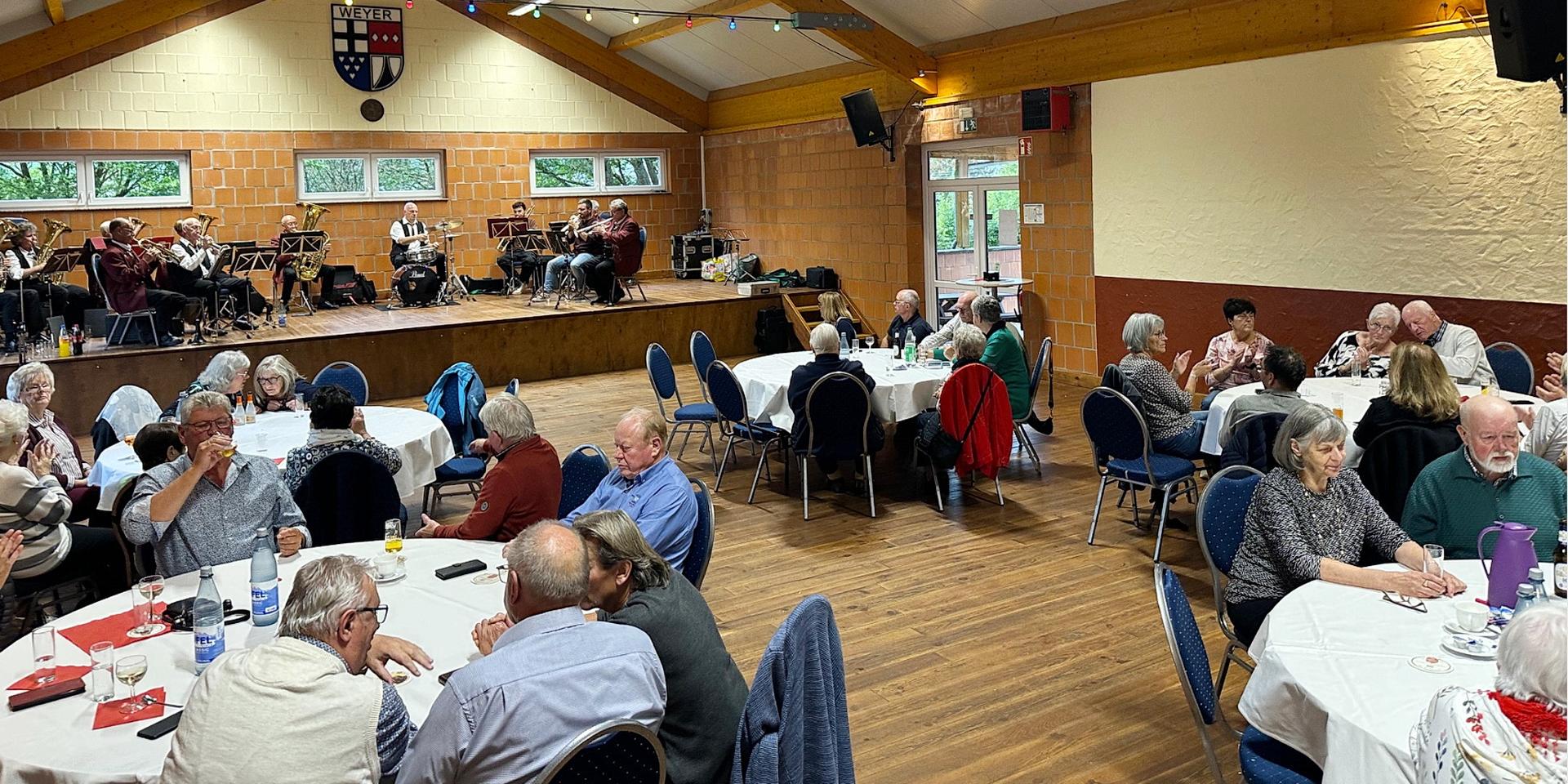 Bei Kaffee, Kuchen und Musik: Zahlreiche Seniorinnen und Senioren genossen den gemütlichen Nachmittag in der Weyerer Bürgerhalle. Im Hintergrund sorgt der Musikverein „Harmonie Weyer“ mit Blasmusik für gute Stimmung.