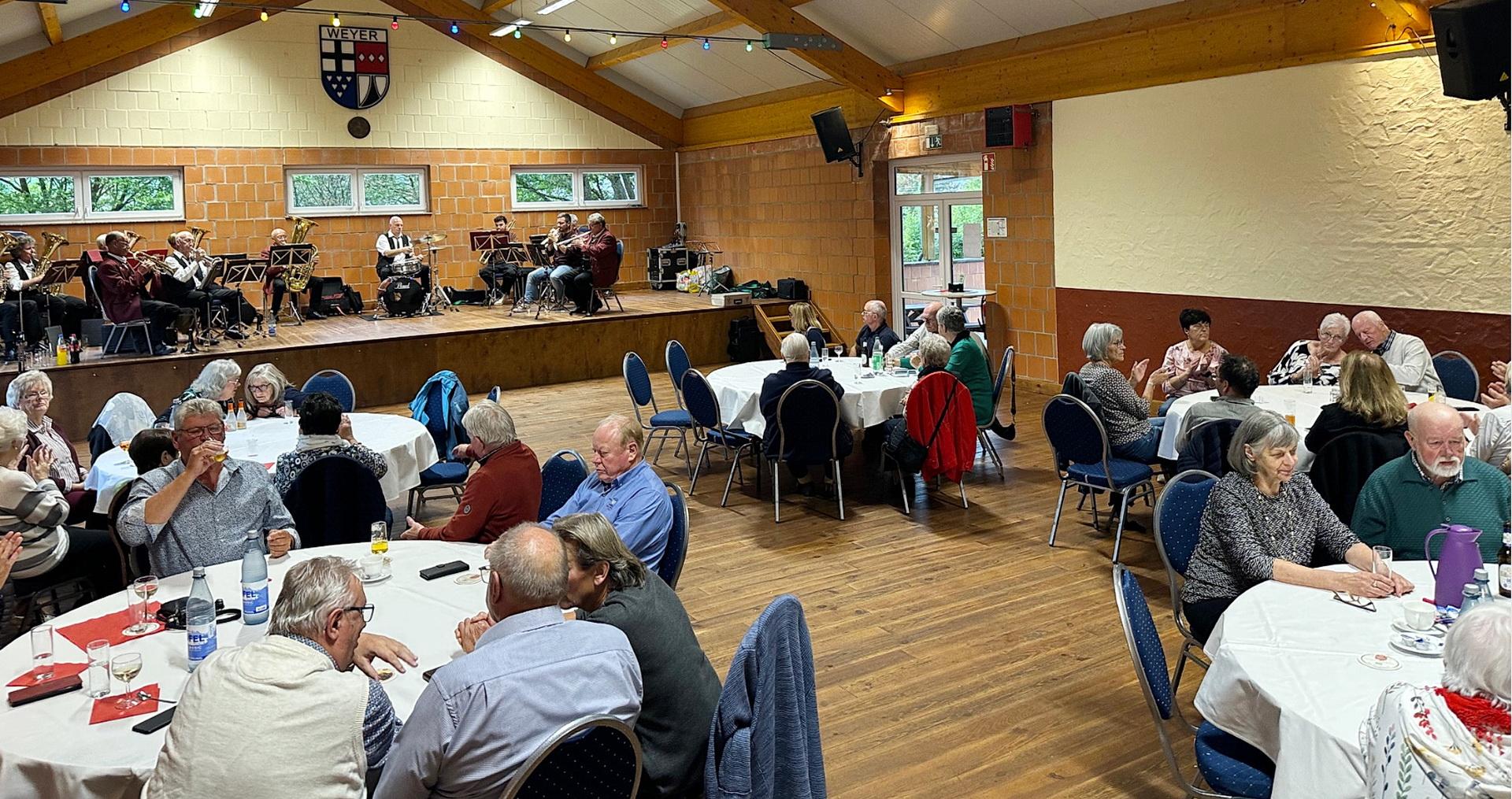 Bei Kaffee, Kuchen und Musik: Zahlreiche Seniorinnen und Senioren genossen den gemütlichen Nachmittag in der Weyerer Bürgerhalle. Im Hintergrund sorgt der Musikverein „Harmonie Weyer“ mit Blasmusik für gute Stimmung.