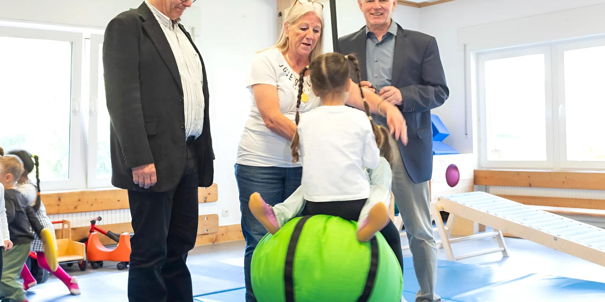 Kinder fliegen durch die Luft angeschubst von Kita-Leiterin Beate Hausmann-Solh. Ralf Claßen (r.) und Dr. Michael Stöhr freuen sich, dass mit der Spende der Mechernich-Stiftung der Schaukelball angeschafft wurde.