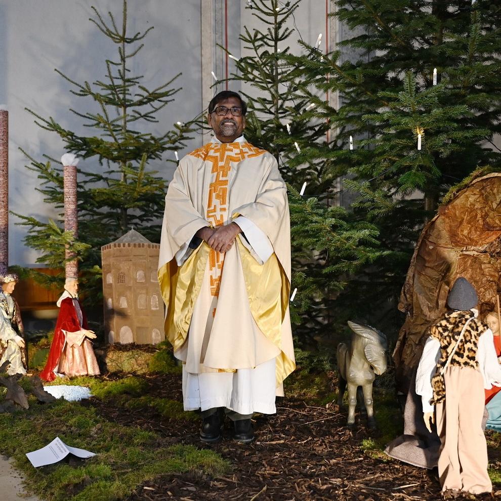 Pfarrer Stephen Rayappan Packiam inmitten der diesjährigen Dreikönigskrippendarstellung in der Pfarrkirche St. Johannes Baptist. Links bei der heranziehenden Karwane sind Malakowturm und die Hüttenschornsteine „Langer Emil“ und „Kurzer Karl“ vom früheren Bergwerksgelände „Op Spandau“ zu erkennen, die Küster Marco Sistig und Gebäudemanager Mario Fuß diese Weihnachten erstmals hinzugefügt haben.