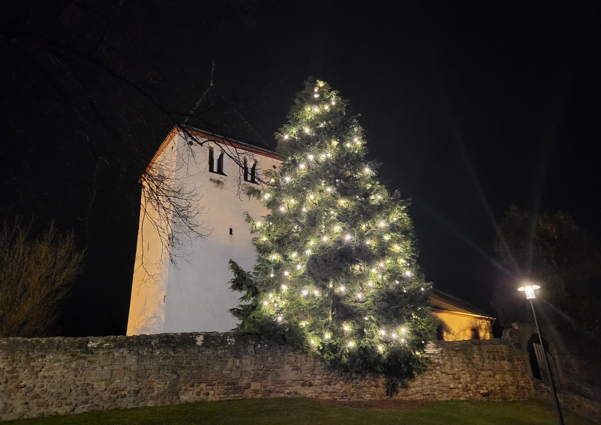 Über den Dächern von Mechernich lässt dieser naturgewachsene Tannenbaum an der Alten Kirche sein warmes Licht erstrahlen. (c) Foto: Manfred Lang/pp/Agentur ProfiPress