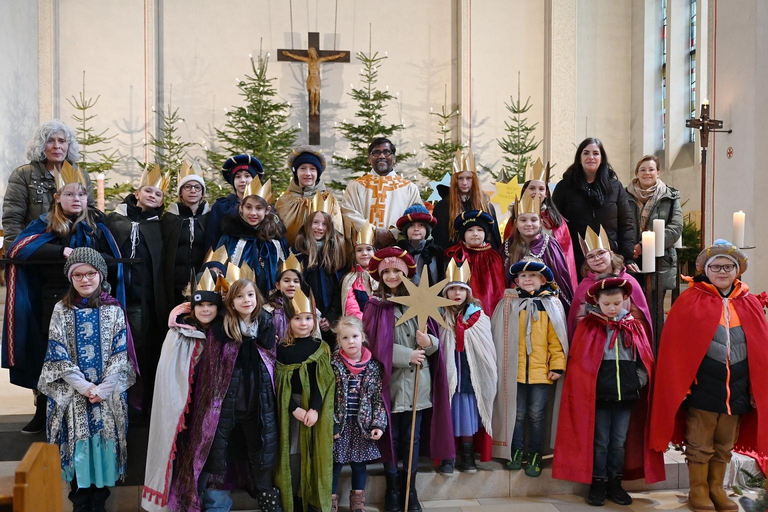 30 der 50 Sternsinger, die in Mechernich und Umgebung den Dreikönigssegen spendeten, Geld für Gleichaltrige in Not sammelten und am Vortag des Dreikönigsfestes in der Mechernicher Pfarrkirche St. Johannes Baptist mit Pfarrer Stephen Rayappan Packiam (m.) Heilige Messe feierten, mit drei Vertreterinnen des tonangebenden Familienmesskreises, links Agnes Peters, rechts Claudia Simon und Ramona Averbeck.